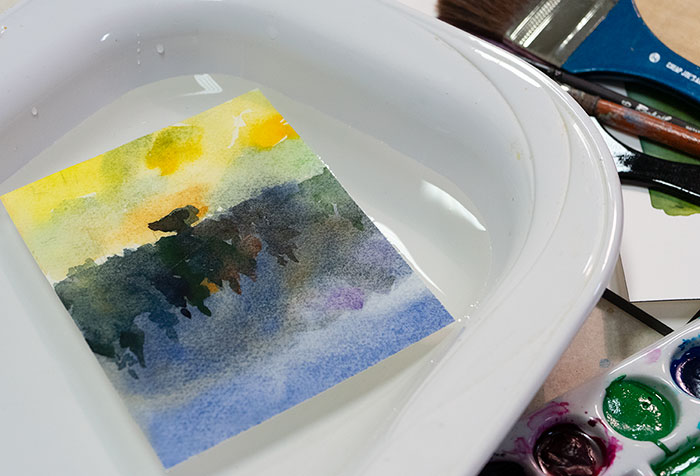 Painted sheet of paper submerged in bowl of water