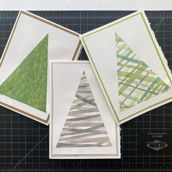 Three handmade watercolor Christmas tree greeting cards with colored borders.